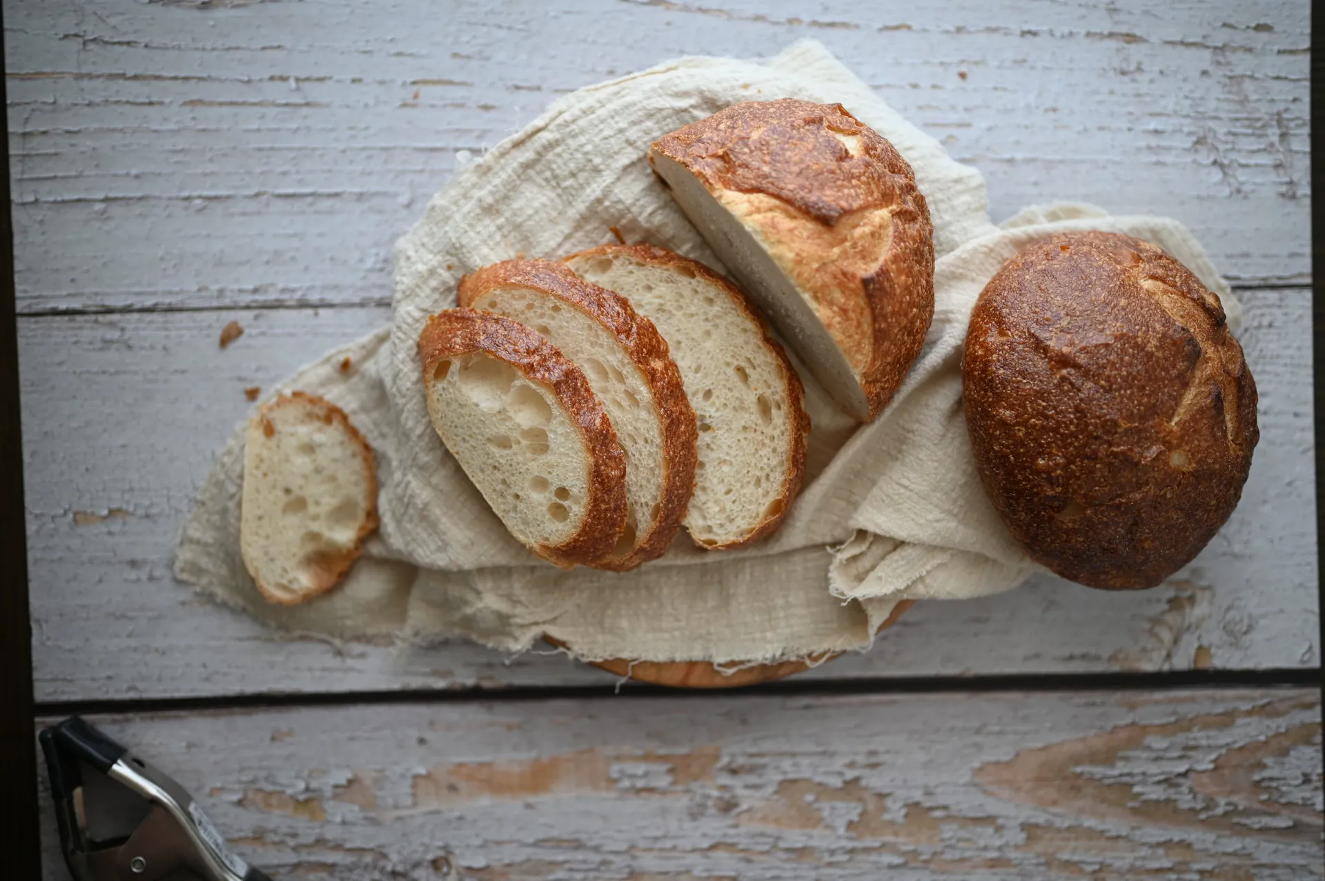 Sliced sourdough and a round loaf on linen, on pale wood (sample photo)
