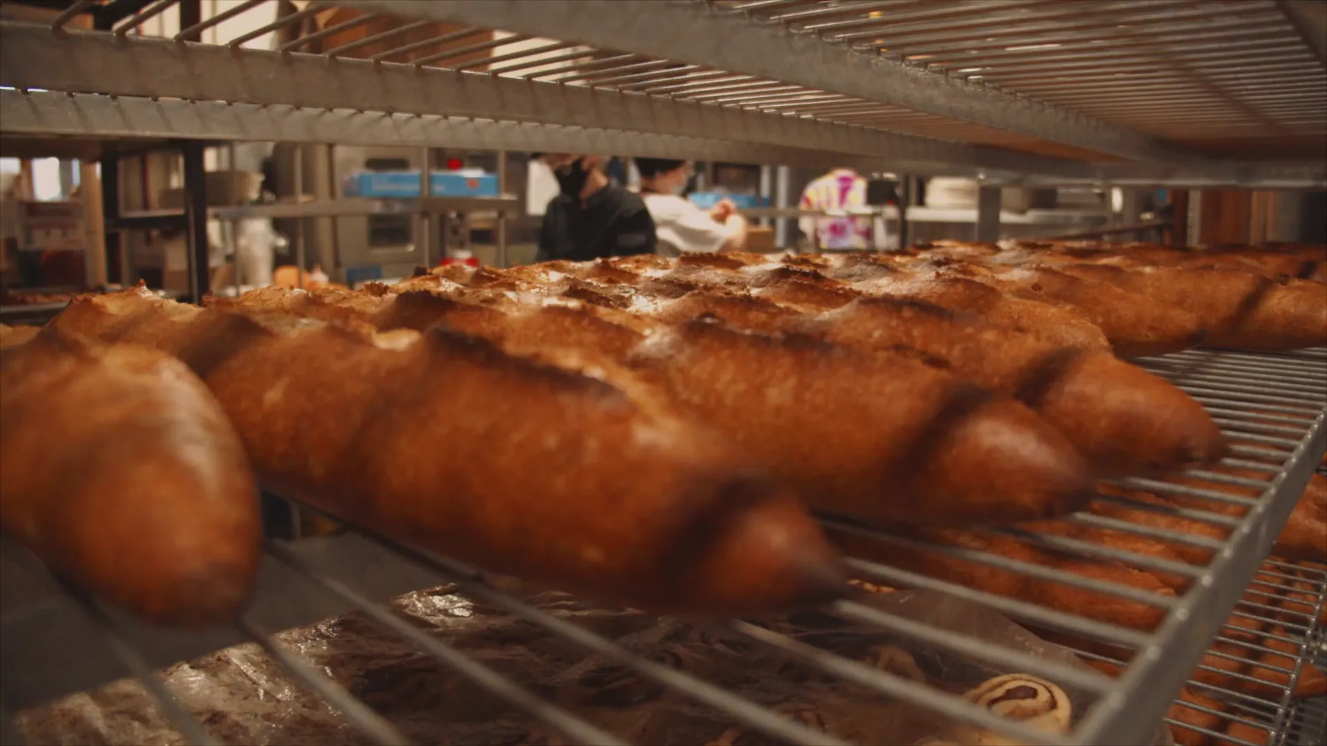 Racks of fresh baguettes in a bakery, bakers busy in the background (sample footage)